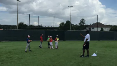 Athletes hold bats on turf and coach explains hitting focus