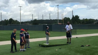 Group of campers watching coach give instruction to pitcher on mound