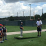 Group of campers watching coach give instruction to pitcher on mound