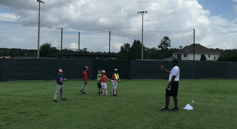 Athletes hold bats on turf and coach explains hitting focus
