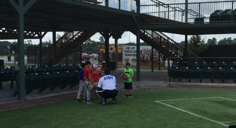 Coach squats to speak with group of campers at Scrap Yard Sports baseball fields