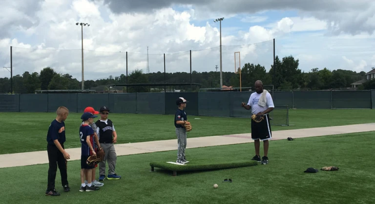 Group of campers watching coach give instruction to pitcher on mound