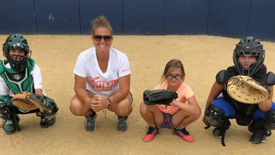 Coach Jamie Wohlbach squats alongside three campers in catcher position