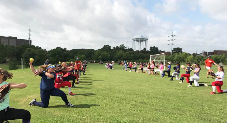 Softball players pair up in the grass to practice throwing while on one knee