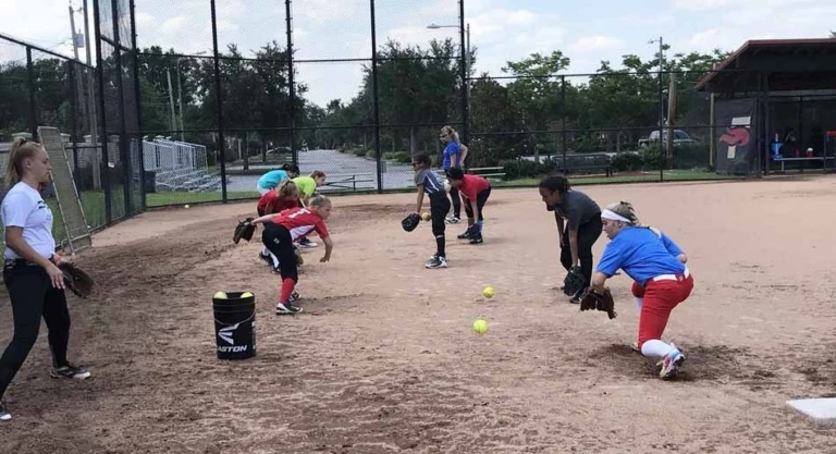 Softball players practice fielding in partners