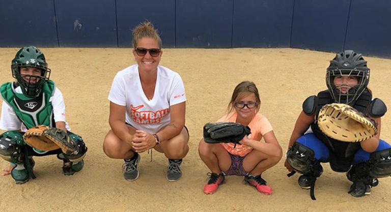 Coach Jamie Wohlbach squats alongside three campers in catcher position